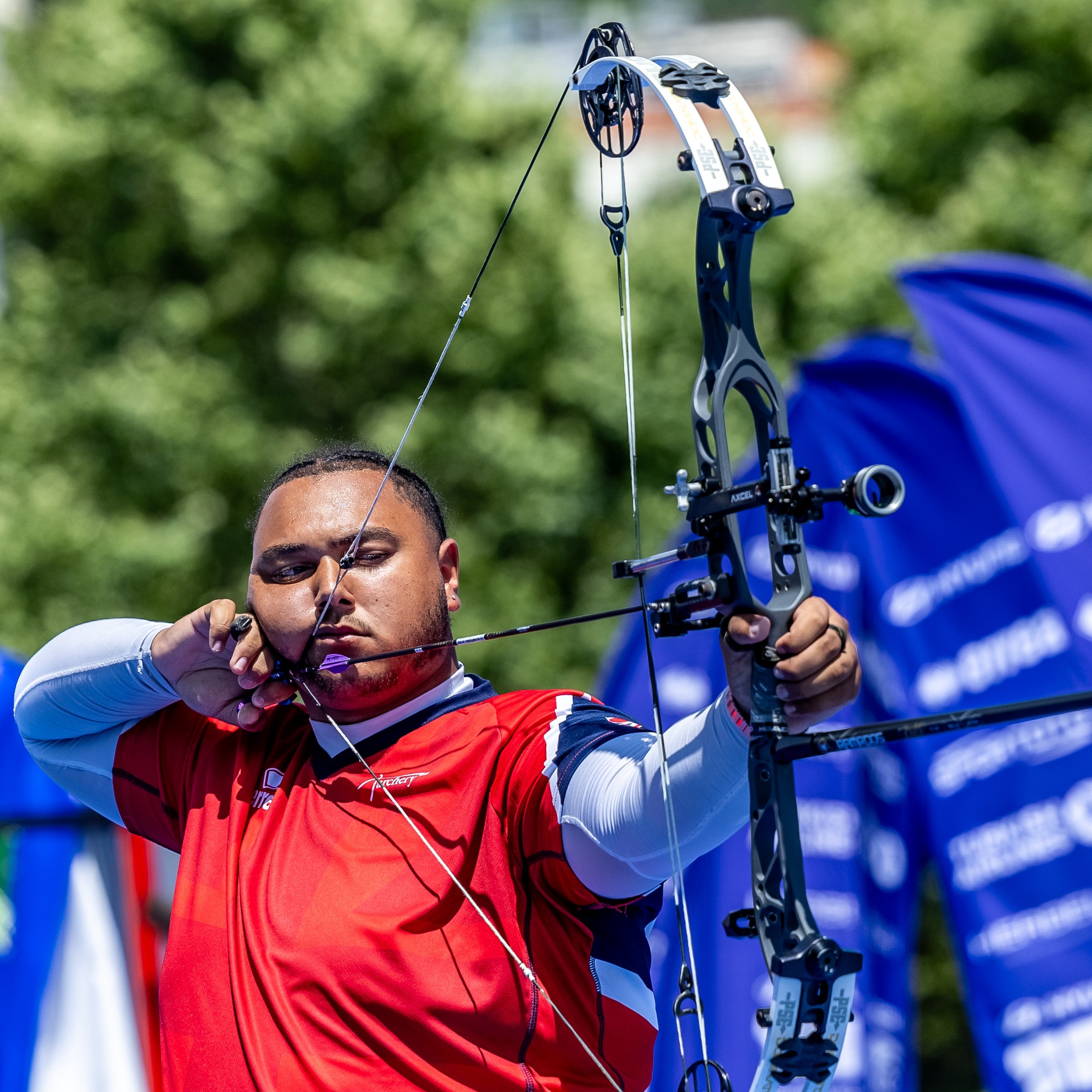 Archer Ajay Scott in red and white outfit with archery equipment, blurred background