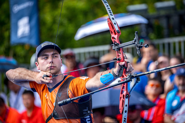 Competitive archer using a compound bow with a long rod stabilizer for enhanced aim and balance during an archery tournament.
